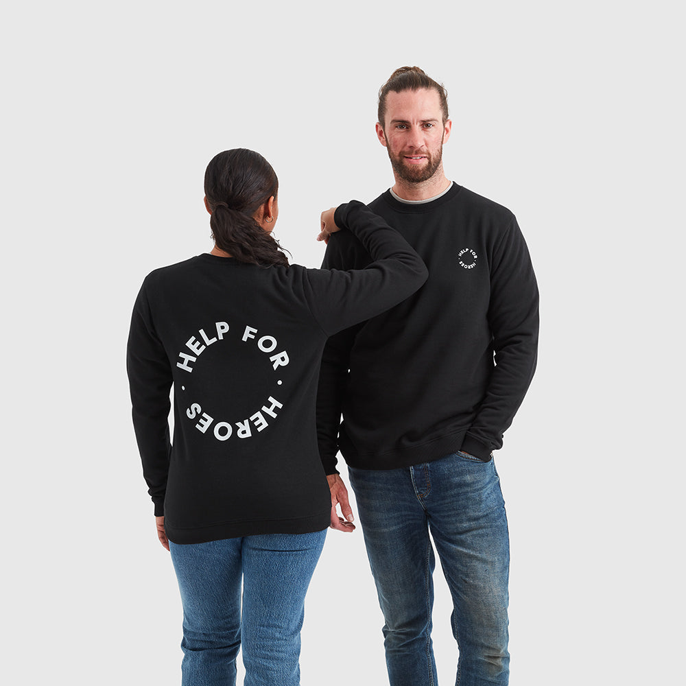Two models wearing black sweatshirt which features a large circular Help for Heroes logo printed on the back and smaller logo printed on the chest