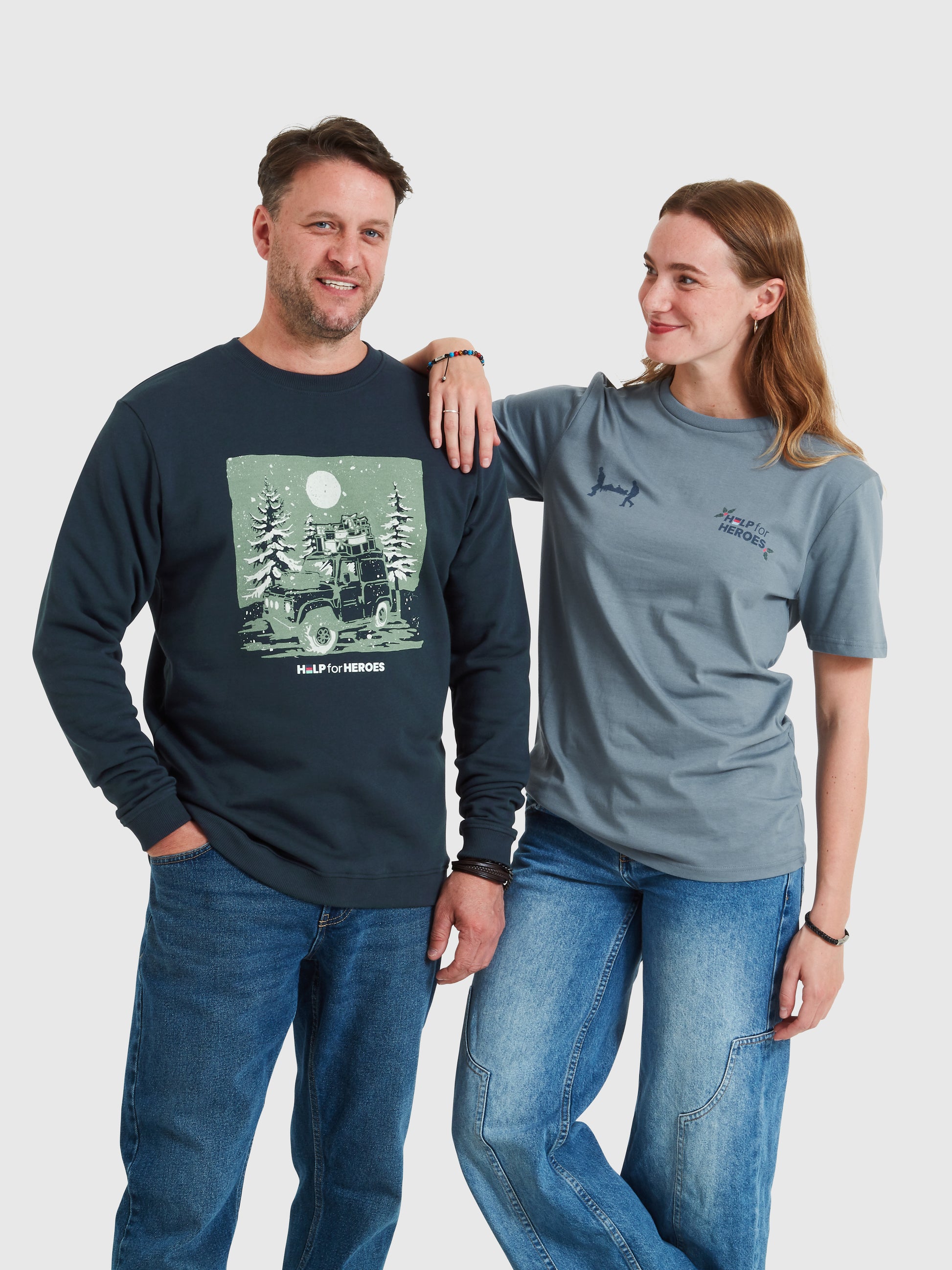 Two Models, male wearing Help for Heroes Christmas sweatshirt, with an image of a Land Rover carrying Xmas presents through a snowy tree scene. Female wearing stone blue t-shirt featuring Xmas Help for Heroes logo and Stretcher Bearer image