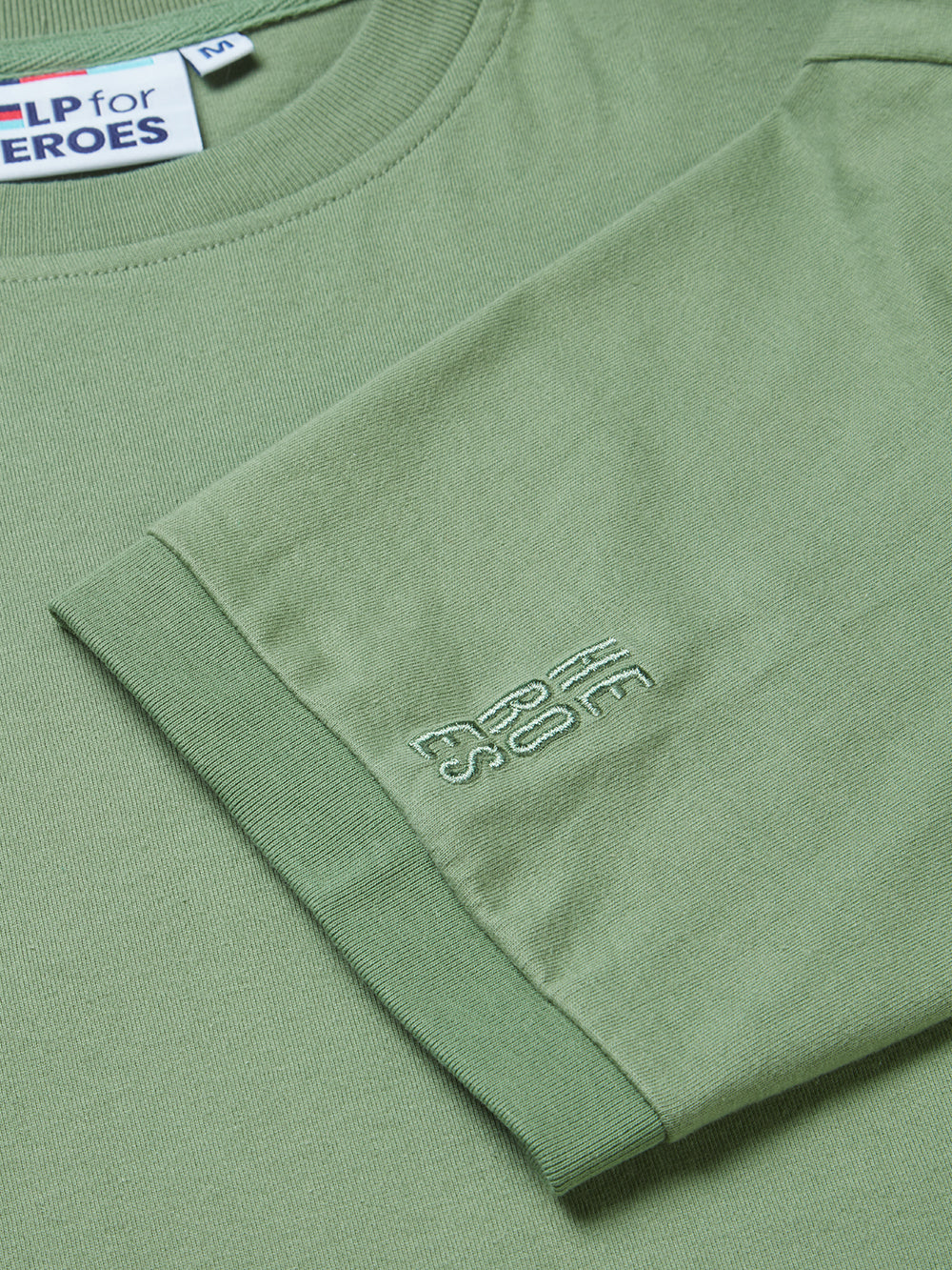 Close up image of embroidered Help for Heroes logo on the sleeve of washed green tshirt