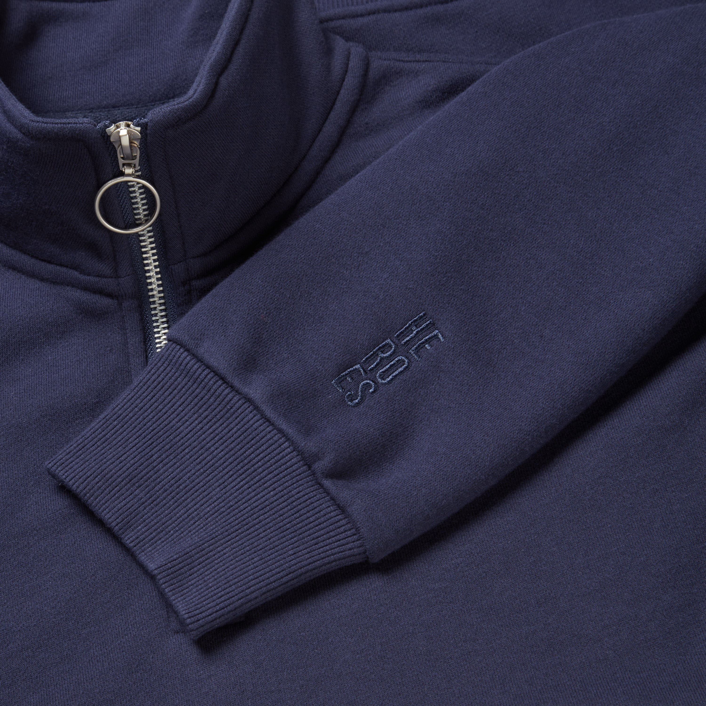Close up image of stacked Help for Heroes logo on the sleeve of half zip sweatshirt in navy