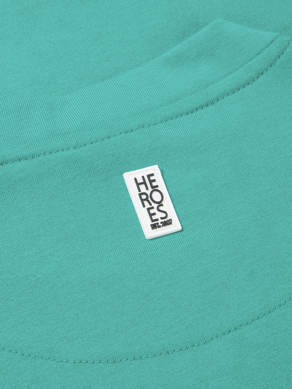 Close up of rubber Help for Heroes logo on back neck of turquoise crew neck tshirt