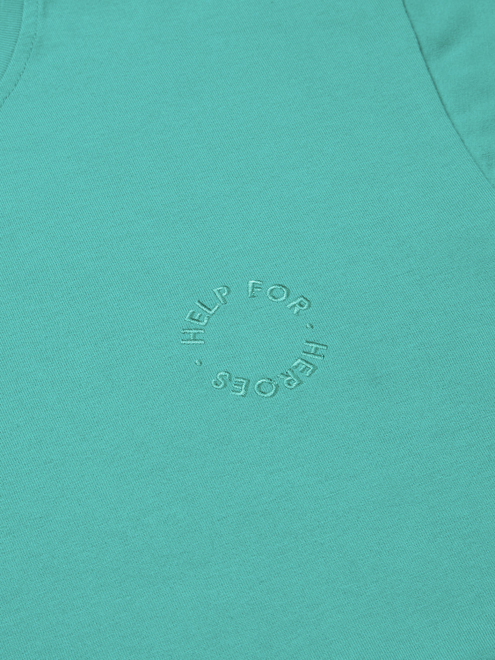 Close up of circular Help for Heroes embroidered logo on turquoise crew neck t-shirt