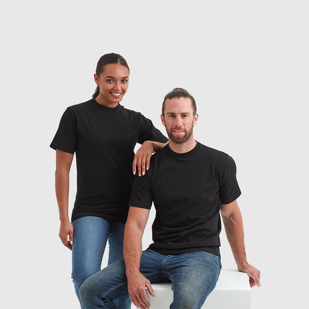 Two models wearing black crew neck t-shirt with a subtle circular Help for Heroes logo on the chest and a rubber Heroes stack patch at the back neck.