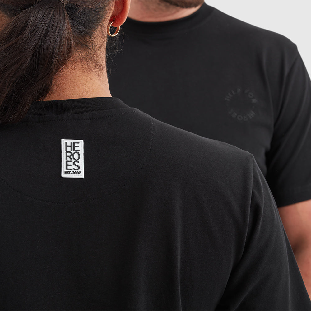 Two models wearing black crew neck t-shirt with a subtle circular Help for Heroes logo on the chest and a rubber Heroes stack patch at the back neck.