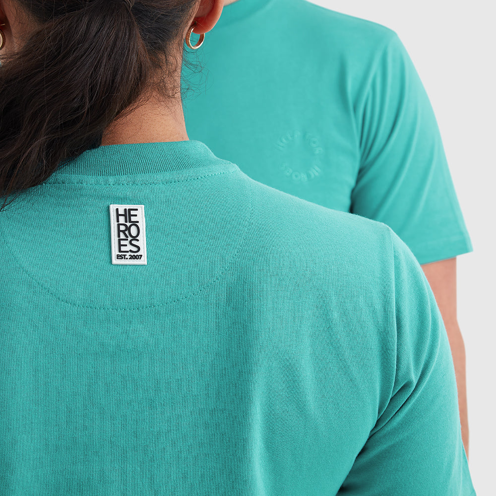 Two models wearing turquoise crew neck t-shirt with a subtle circular Help for Heroes logo on the chest and a rubber Heroes stack patch at the back neck.