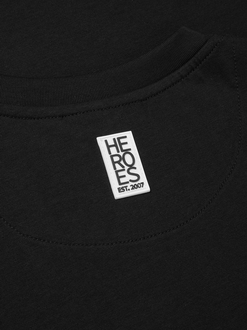 Close up image of rubber Help for Heroes logo on back neck of black crew neck t-shirt