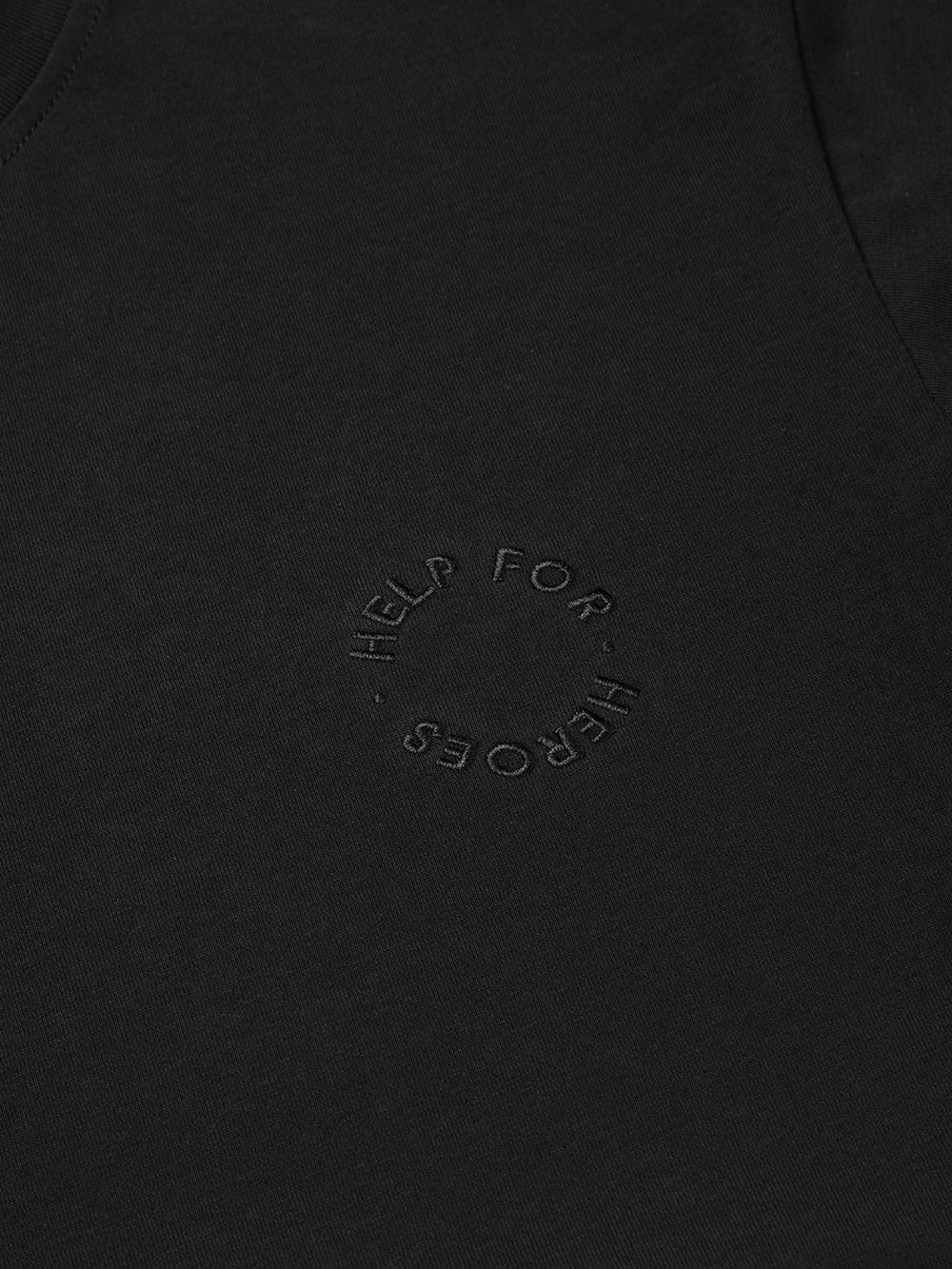 Close up image of circular embroidered Help for Heroes logo on the chest of black crew neck t-shirt