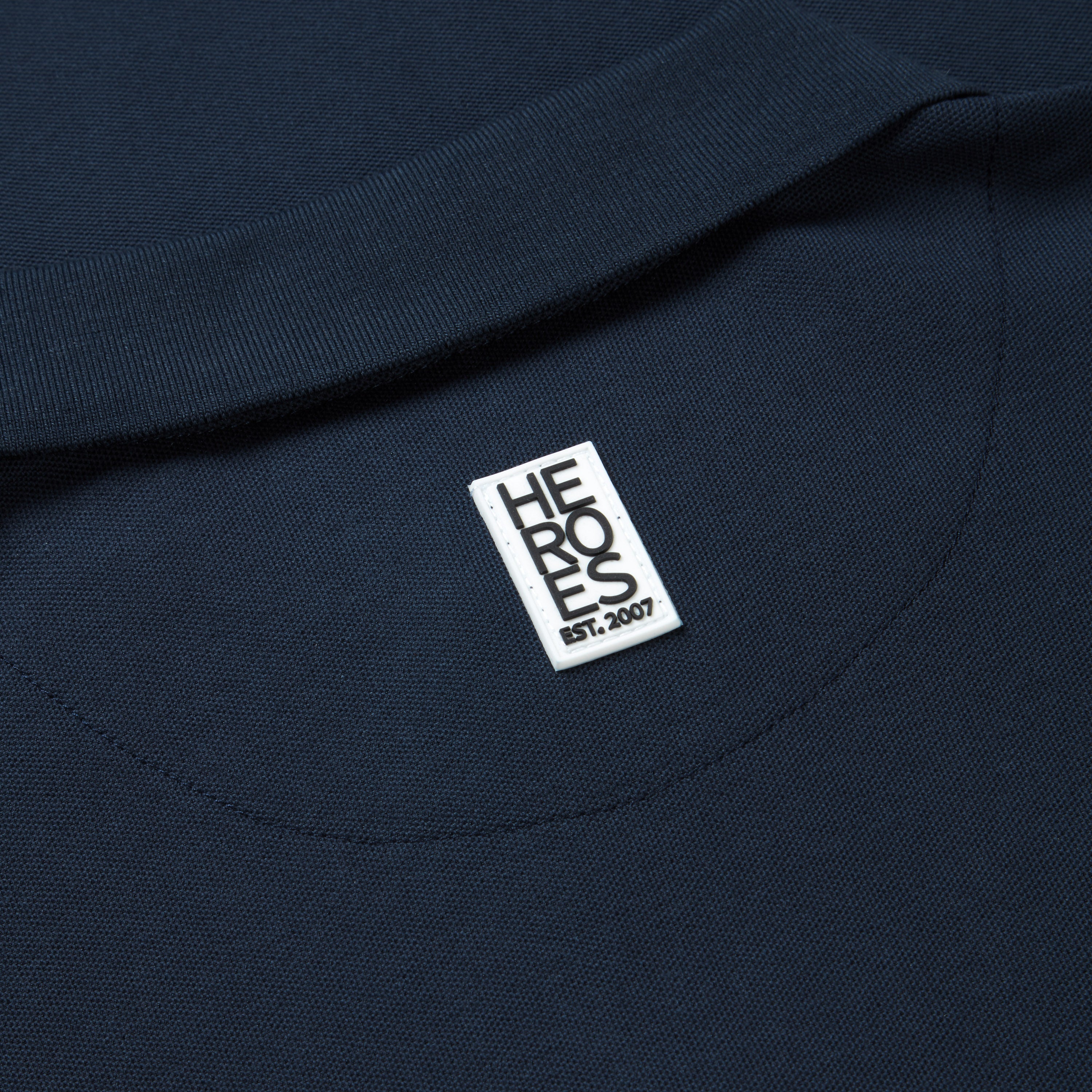 Close up image of rubber Help for Heroes logo on back next of the navy pique polo