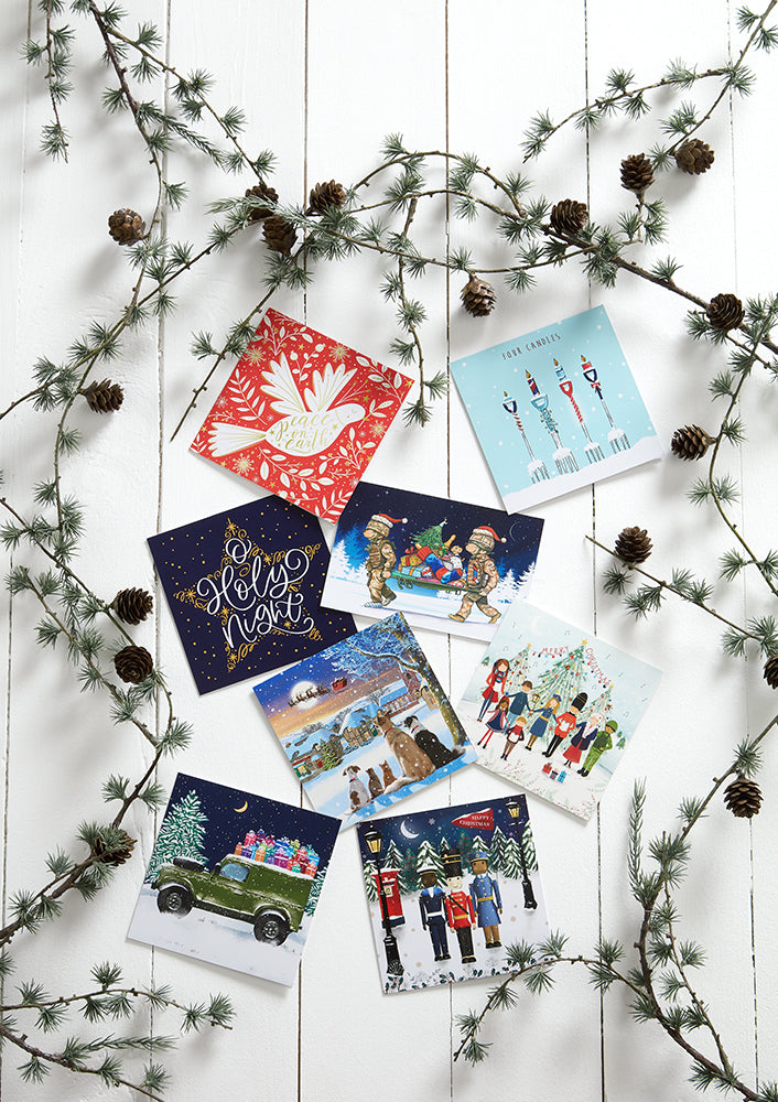 Collection of Christmas cards on a white wooden surface with pine branches.