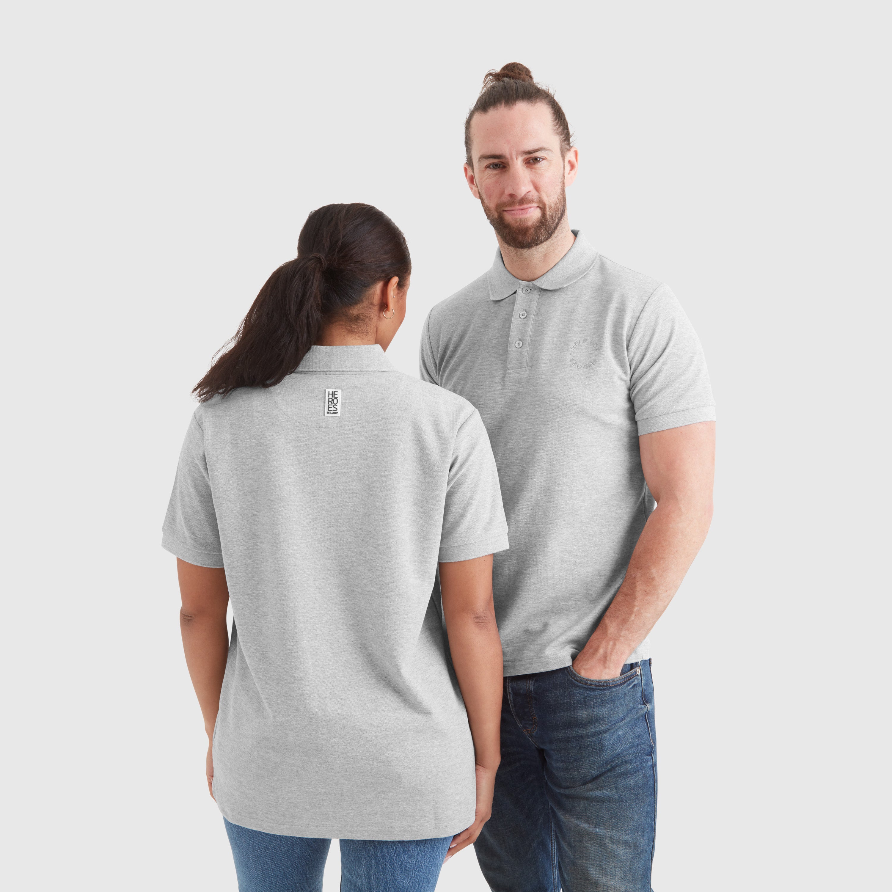 Two models wearing grey marl pique polo shirts with a subtle circular Help for Heroes logo on the chest and a rubber Heroes stack patch at the back neck.