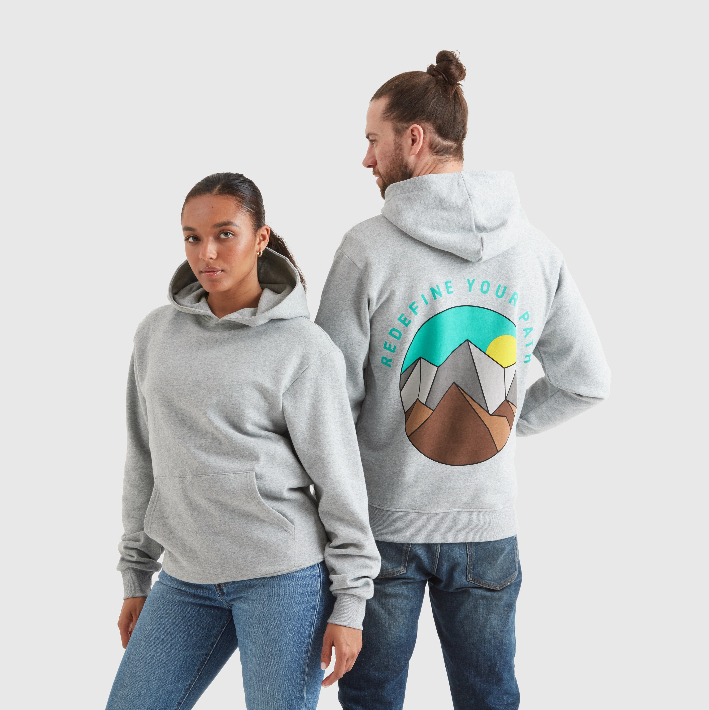 Two models wearing a grey marl pullover hoodie with the text "redefine your path" and a mountain scene back print' featuring a circular Help for Heroes logo on the sleeve