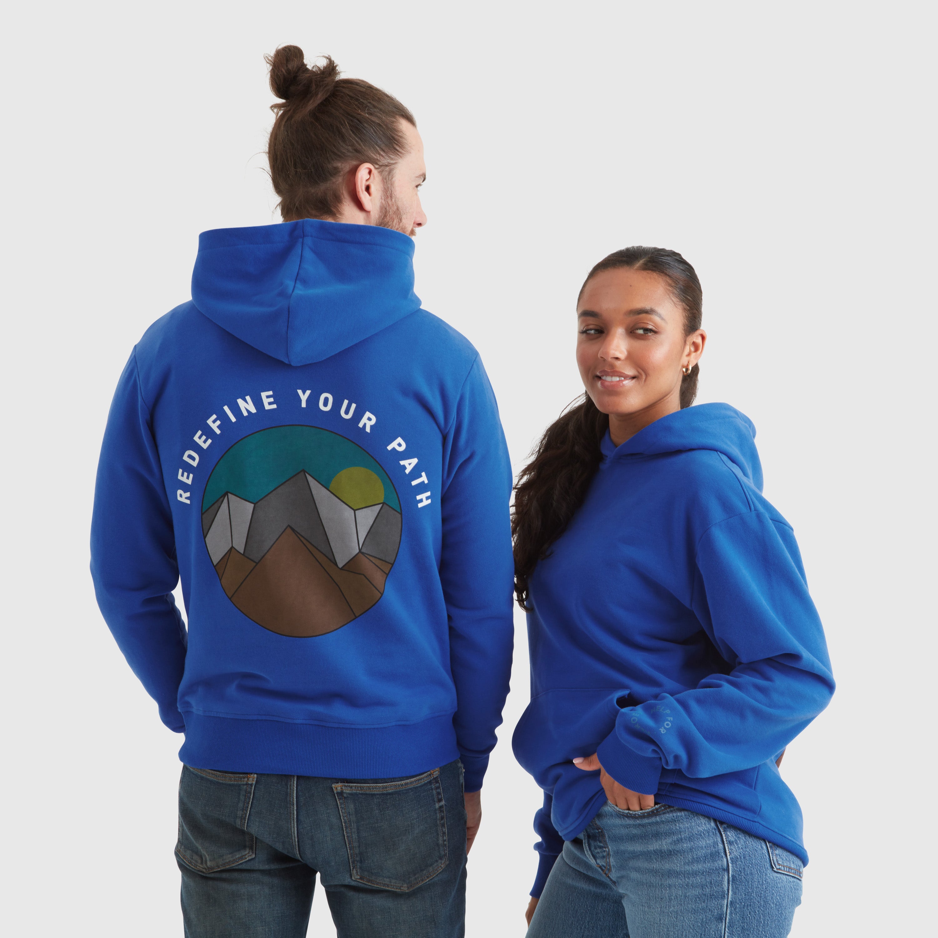 Two models wearing blue pullover hoodies with the text "redefine your path" and a mountain scene back print featuring a circular Help for Heroes logo on the sleeve