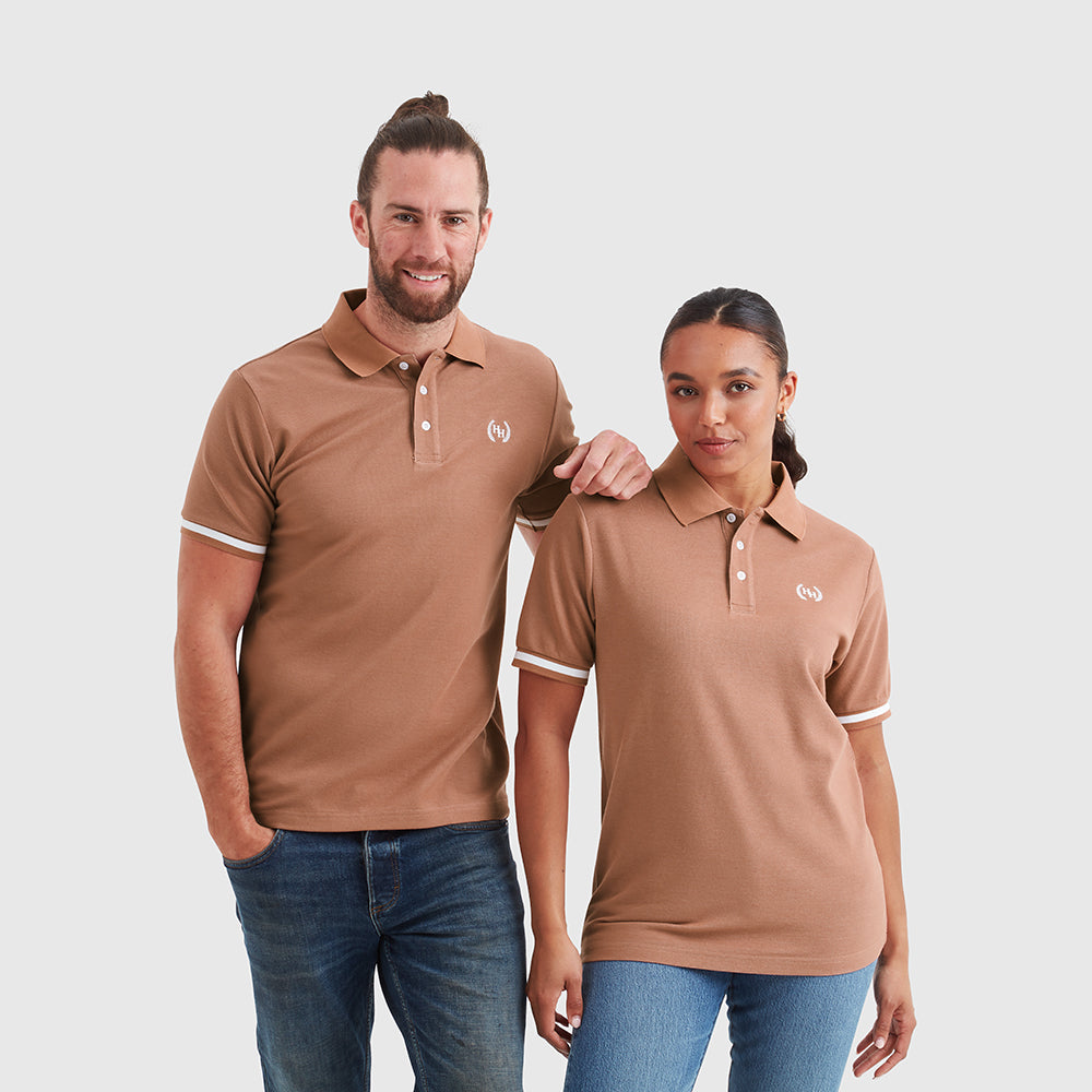 Two models wearing a mocha pique fabric polo shirt with an embroidered help for heroes wreath logo on the chest, tipping on the cuffs, and branded buttons.