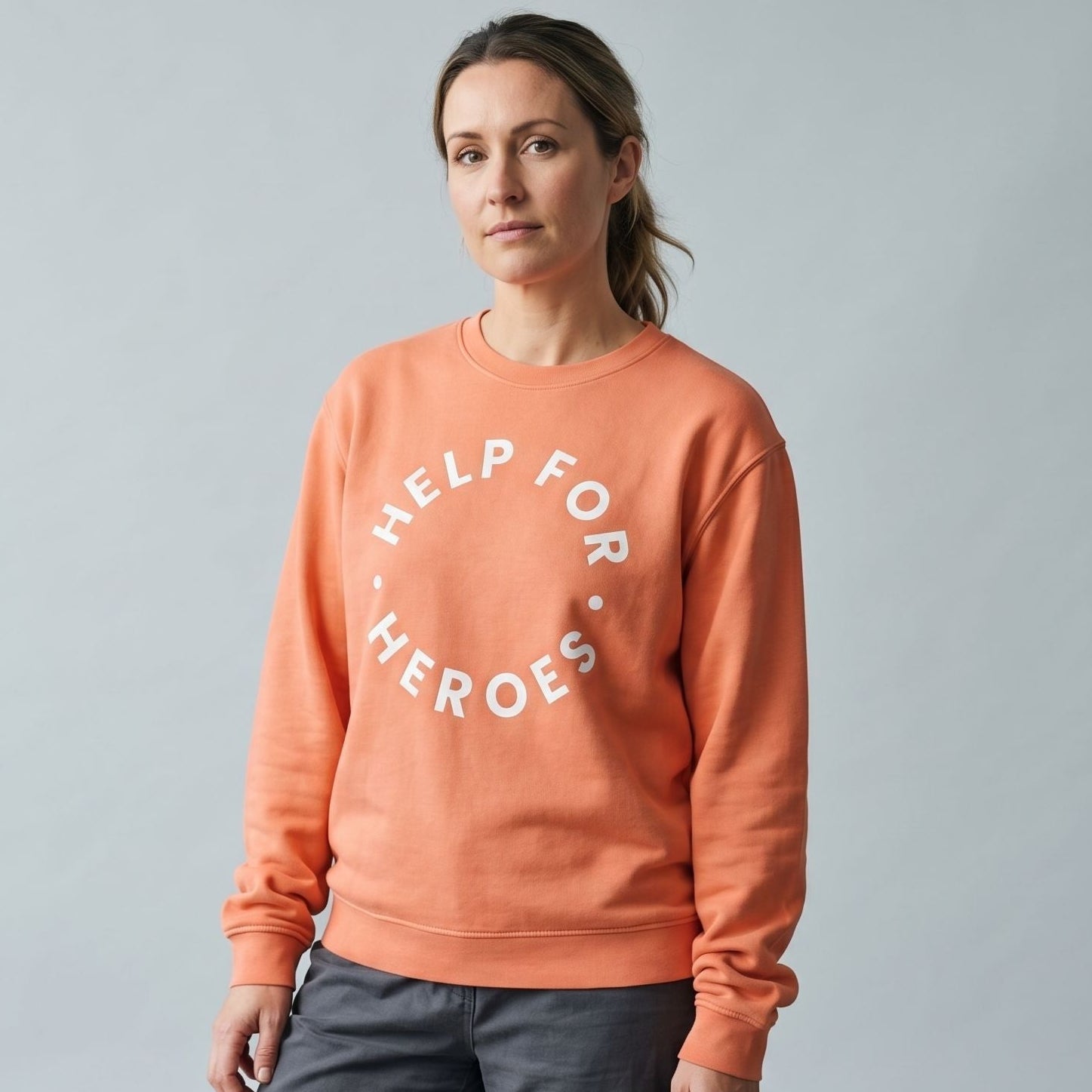 Model wearing a soft orange sweatshirt with a white Help for Heroes logo on the front