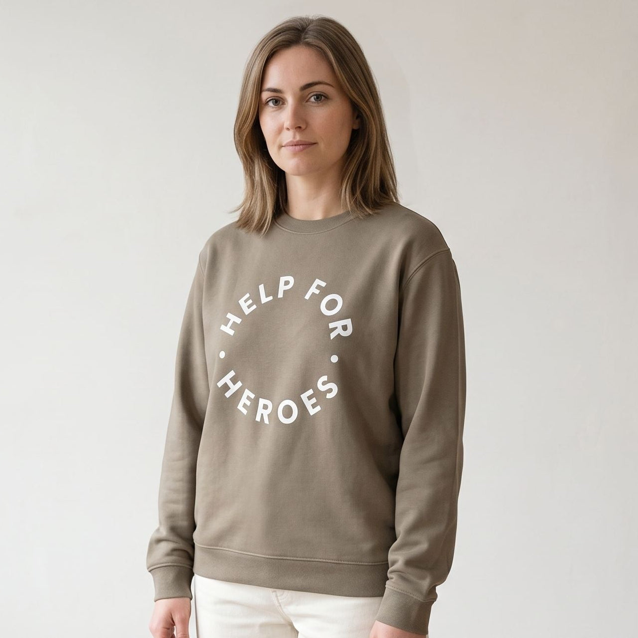 Model wearing a Help for Heroes sweatshirt in a soft brown colour with a white circular logo print on the front