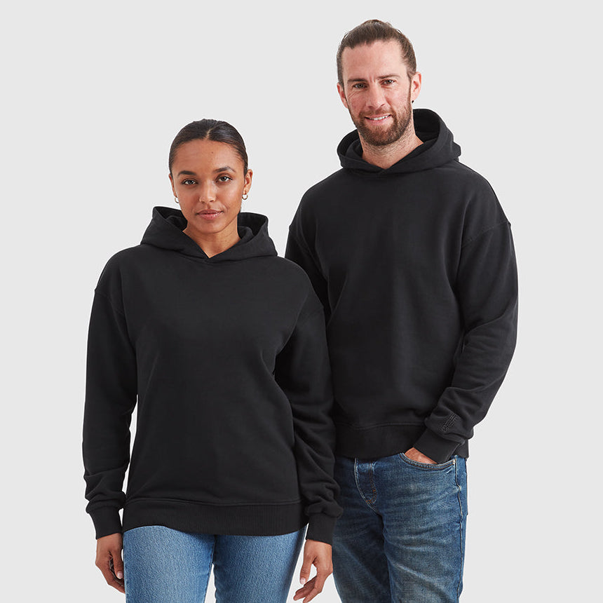 Two models wearing relaxed fit pullover black hoodie. Featuring a subtle embroidered Help for Heroes logo on the sleeve