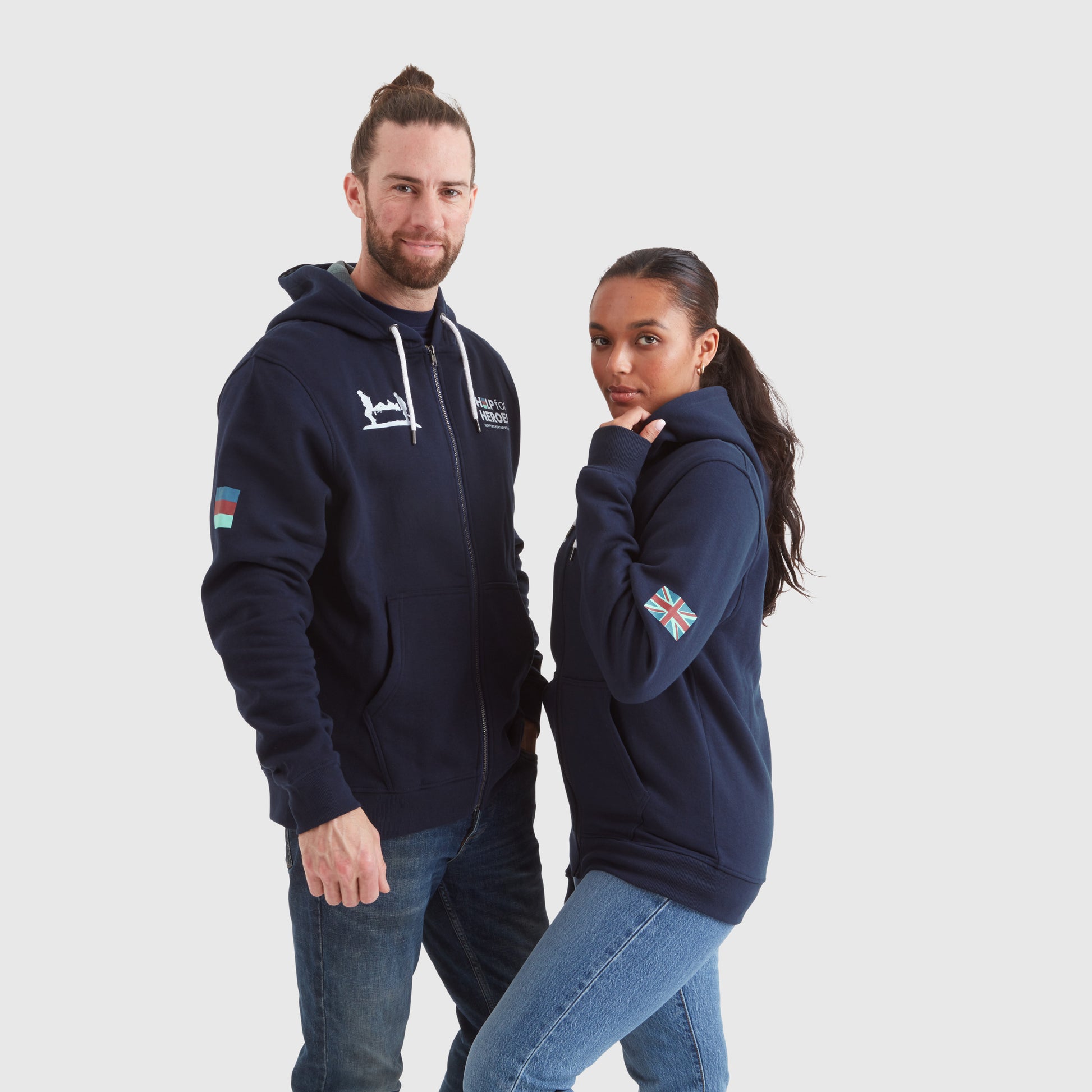 A male and a female model wearing navy zip hoodies with the 'Help for Heroes' logo, Stretcher Bearer and Union Jack and Tri Colour flag prints.
