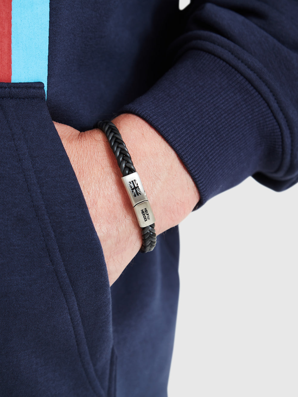 Help for heroes grey slim plaited bracelet, with metal clasp featuring union jack, worn on model's wrist. 