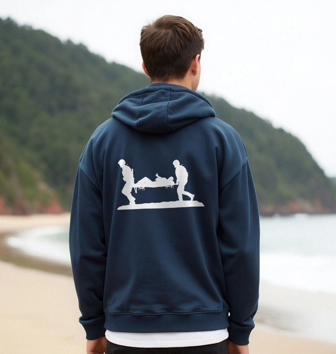 Person wearing a Help for Heroes navy blue hoodie with a white graphic on the back, standing on a beach.