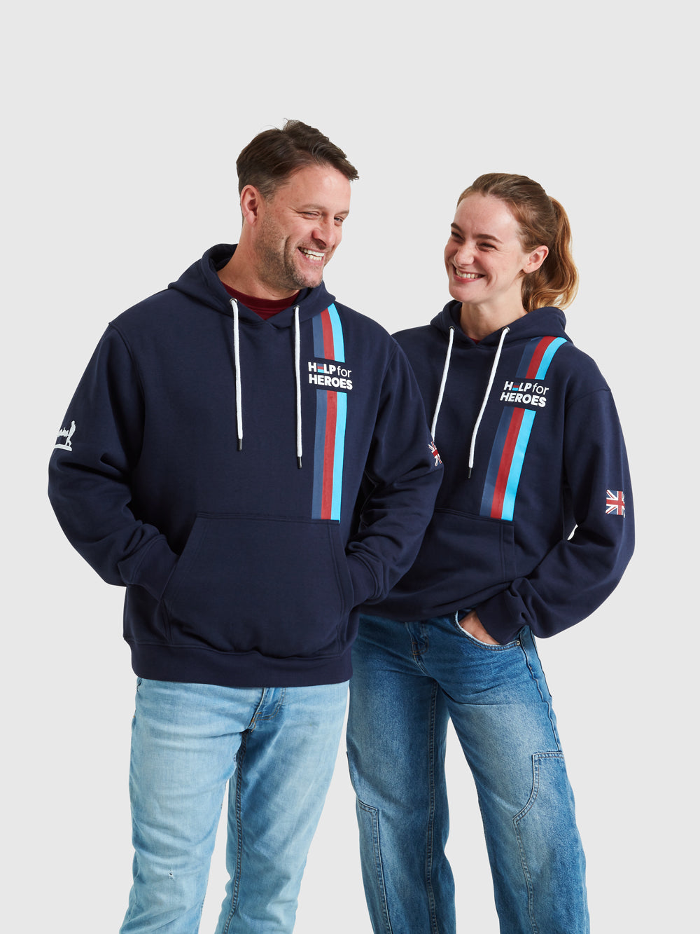 Two models wearing navy pullover hoodies which feature the Help for Heroes logo and tri colour stripe. Printed Union Jack flag on one sleeve and Stretcher Bearer logo on other sleeve